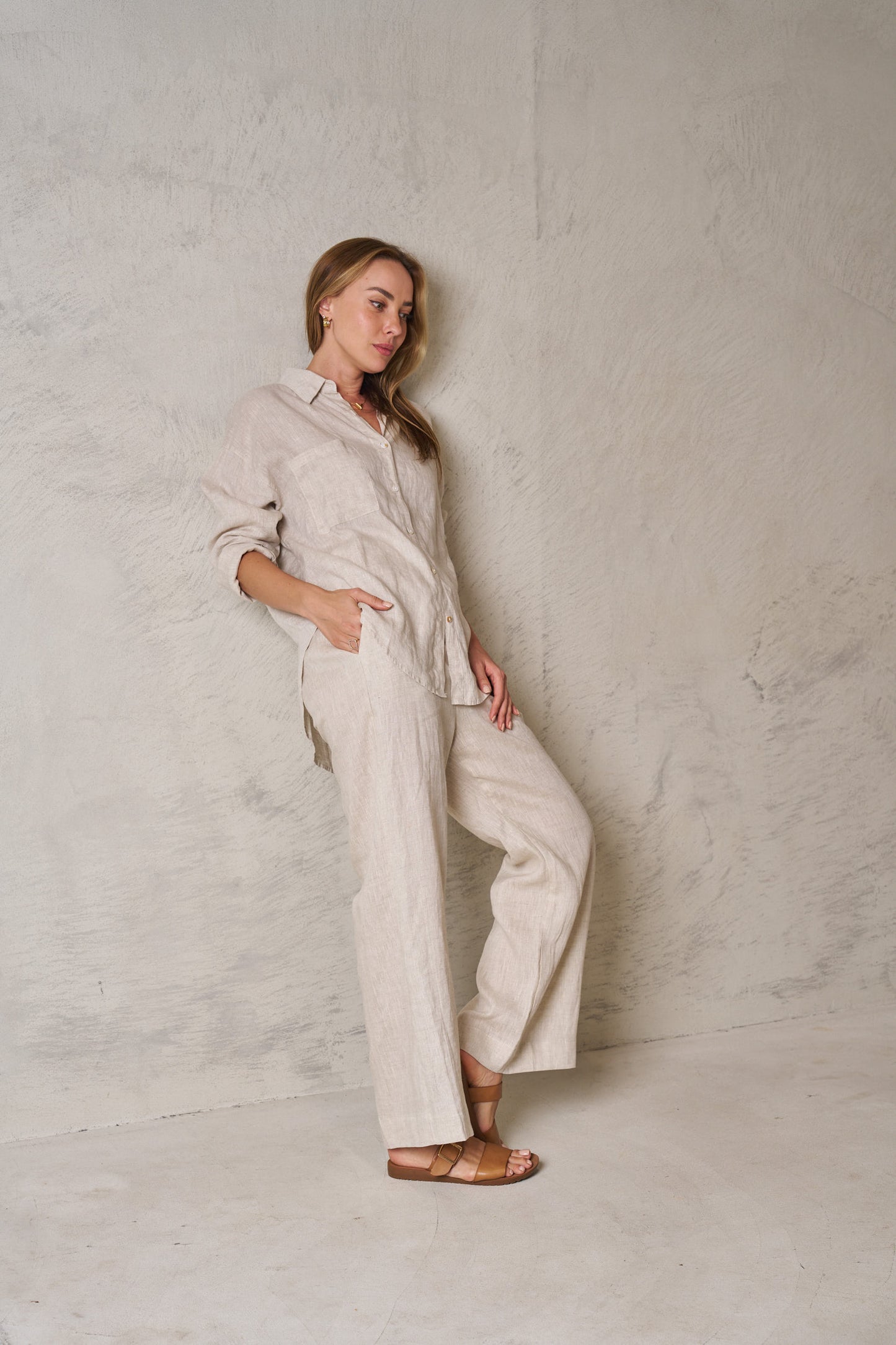 Woman wearing a light-colored linen outfit against a textured white wall.
